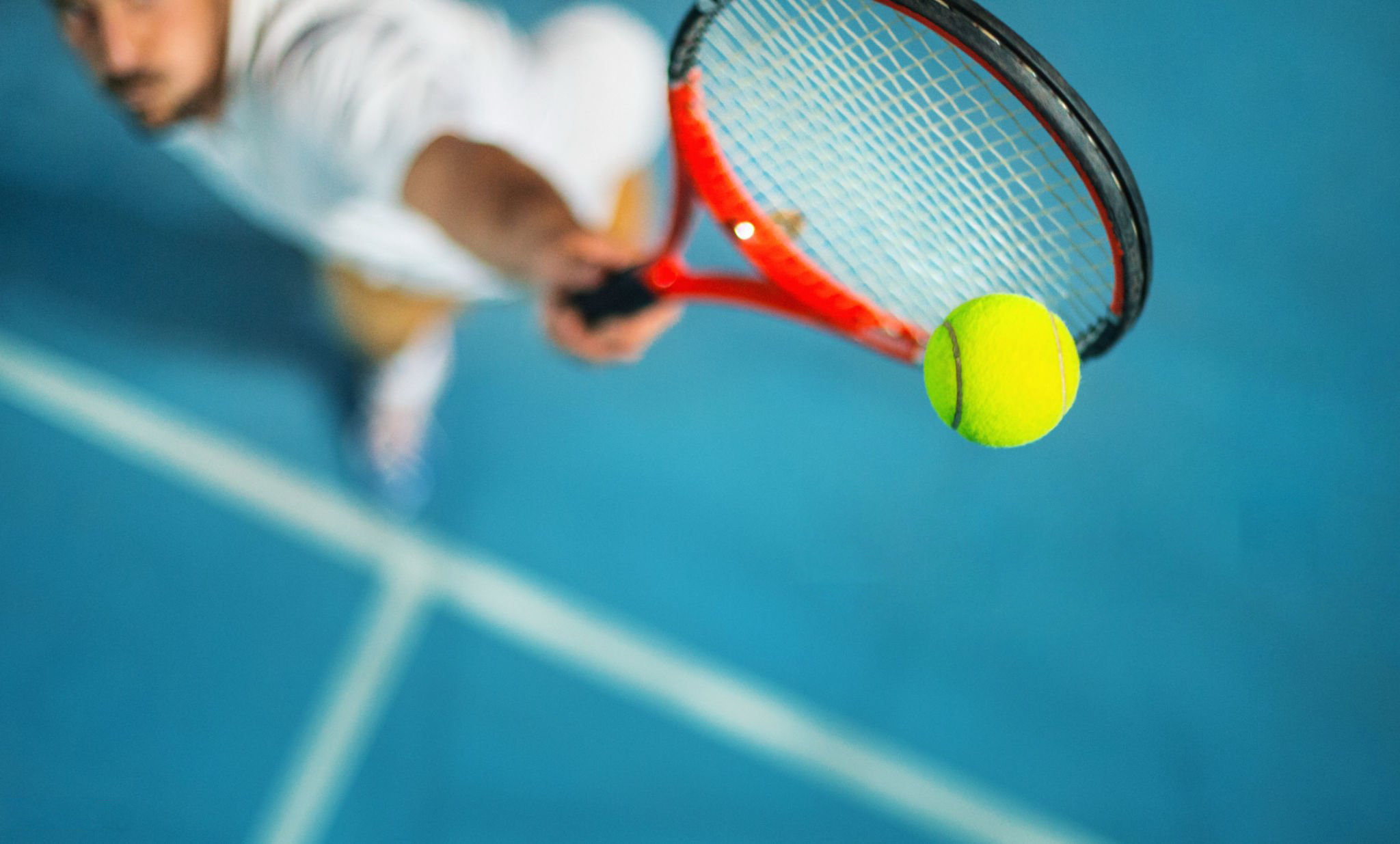 Closeup high angle view of two male tennis player competing in an outdoors night match. He's hitting a serve or a volley against blue hard court with copy space.