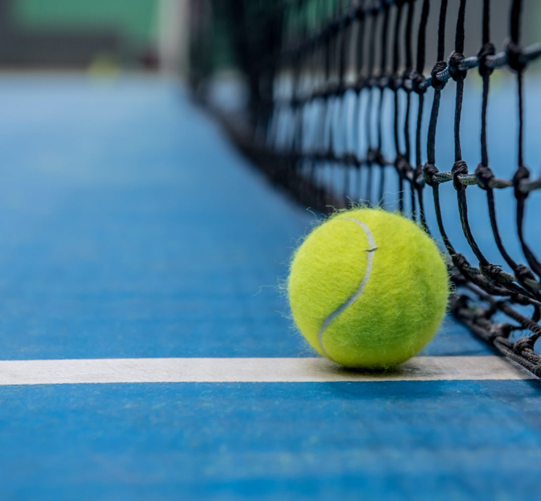 Yellow tennis ball on blue hard court surface with black net