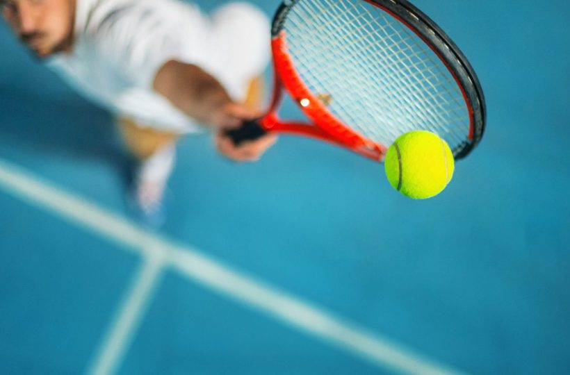 Closeup high angle view of two male tennis player competing in an outdoors night match. He's hitting a serve or a volley against blue hard court with copy space.